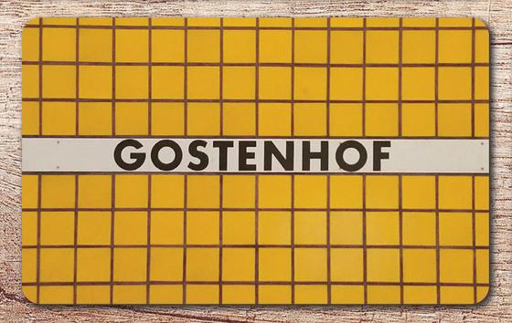 U-Bahnhof Gostenhof Frühstücksbrettchen - weißes Schild mit schwarzer Schrift auf gelbem Fliesenhintergrund