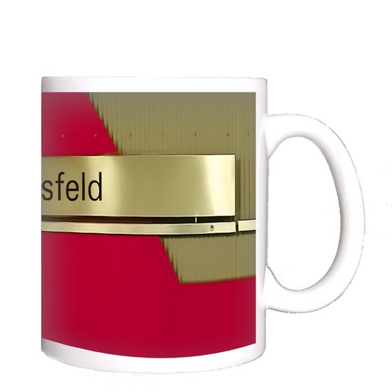U-Bahnhof Moosfeld Kaffeetasse - schwarze Schrift auf goldenem Schild, vor rotem Untergrund mit grünlichen Elementen