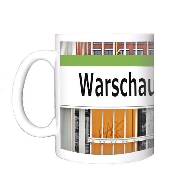 U-bahnhof Warschauer Straße Kaffeetasse - schwarze Schrift auf weißem Schild, mit grasgrünem Streifen, angebracht an einem Zaun, vor einfahrender gelber U-Bahn