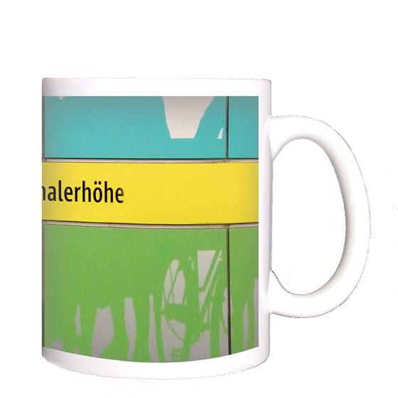 U-Bahnhof Schwanthalerhöhe Kaffeetasse - schwarze Schrift auf gelbem Streifen, zwischen grünem und blauem Querstreifen mit abstrakten Mustern