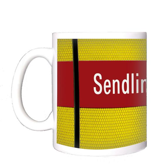 U-Bahnhof Sendlinger Tor Kaffeetasse - weiße Schrift auf rotem Streifen, vor gelbem Raster, durchzogen von schwarzem Senkrechtstreifen