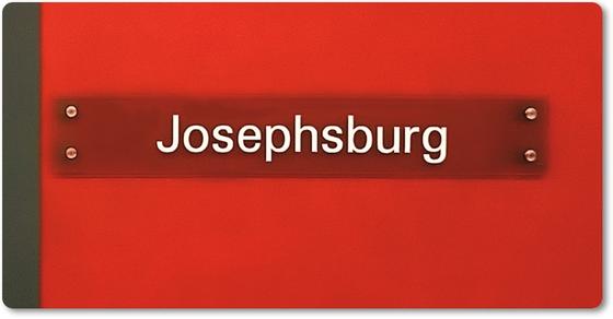 U-Bahnhof Josephsburg - weiße Schrift rötlich-braunem Streifen vor mohnrotem Hintergrund