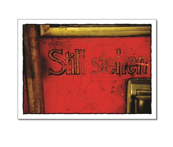 Klassische  Postkarte - Verschnaufpause. Foto des Schriftzuges "Still stehen" gedruckt auf einen roten Untergrund. 