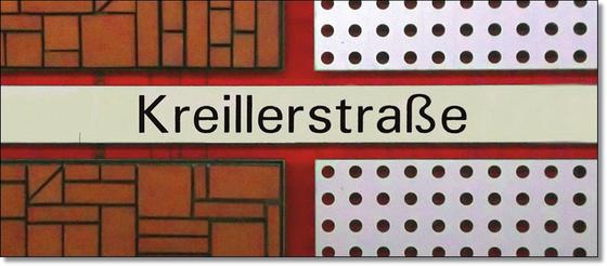 U-Bahnhof Kreillerstraße Kaffeetasse - schwarze Schrift auf weißem Schild, welches Teil eines roten Kreuzes ist, vor zweigeteiltem Hintergrund mit schwarz-weißen Punkten und rot-braunem Backsteinmuster