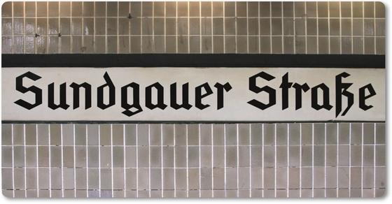 S-Bahnhof Sundgauer Straße, S-Bahnhof, Souvenirshop, Stadtrundfahrt, Berliner U-Bahn Magnet - schwarze Frakturschrift auf weißem Schild mit schwarzem Streifen, auf grau-braunem Fliesenhintergrund