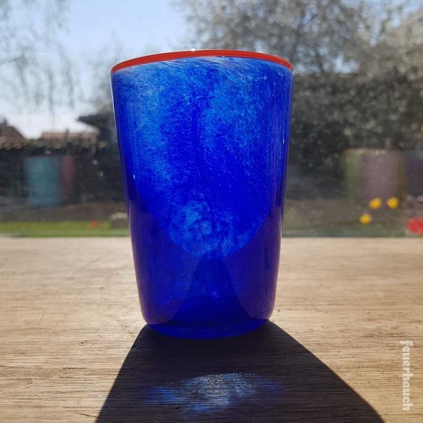 Mundgeblasenes Trinkglas aus dem Glasstudio Feuerhauch in blau und mit gelb-orangenen Rand, Unikat, Teelicht, im Sonnenlicht